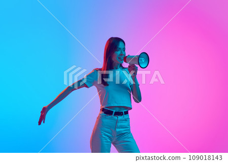 Young woman in casual clothes talking in megaphone against gradient pink blue studio background in neon light 109018143