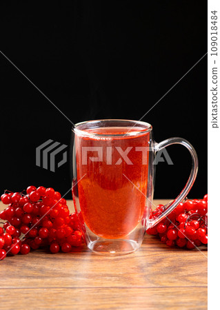 Hot viburnum tea in a glass cup with a double bottom on a black background. Hot viburnum tea in a glass cup with a double bottom on a black background. 109018484