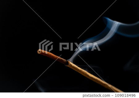 Smoke from a burning aroma stick on a black background. Incense sticks, aromatherapy and meditation. Smoke from a burning aroma stick on a black background. Incense sticks, aromatherapy and meditation. 109018496