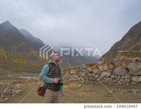 A male tourist takes pictures of a beautiful autumn mountain foggy landscape using a camera. A male tourist takes pictures of a beautiful autumn mountain foggy landscape using a camera. 109018497