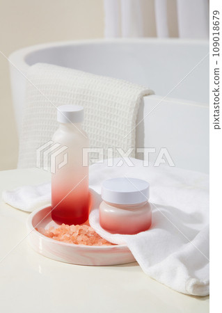 Rounded marble tray with a blank label bottle and jar placed on. A handful of pink himalayan salt displayed. Background with a bathtub with white towel hanging on. Branding mockup Rounded marble tray with a blank label bottle and jar placed on. A handful of pink himalayan salt displayed. Background with a bathtub with white towel hanging on. Branding mockup 109018679