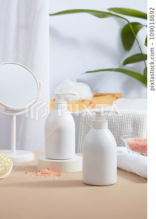 Two pump bottles without label featured on the table with a mirror, scalp massage brush and folded towel with a jar of pink himalayan salt placed on. Blank label bottle for mockup design Two pump bottles without label featured on the table with a mirror, scalp massage brush and folded towel with a jar of pink himalayan salt placed on. Blank label bottle for mockup design 109018692