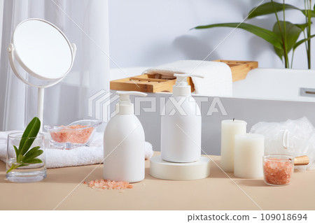 Many bathroom supplies featured on beige table with glass container of pink himalayan salt and unlabeled pump bottles. Himalayan salt is becoming increasingly popular due to its therapeutic properties Many bathroom supplies featured on beige table with glass container of pink himalayan salt and unlabeled pump bottles. Himalayan salt is becoming increasingly popular due to its therapeutic properties 109018694