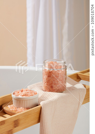 Close up view of a bowl and transparent jar containing pink himalayan salt placed on a wooden bathtub tray. Pink himalayan salt is a brilliant natural exfoliator Close up view of a bowl and transparent jar containing pink himalayan salt placed on a wooden bathtub tray. Pink himalayan salt is a brilliant natural exfoliator 109018704