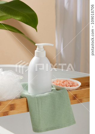 Pump bottle in white color decorated with a bath sponge and a small dish of pink himalayan salt. White cosmetic bottle for face cream, cleanser, body lotion or shampoo 109018706