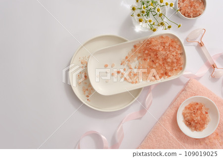 Pink himalayan salt divided on many different plates, decorated with pink ribbon, flowers pot and facial massage roller. Blank space for text adding Pink himalayan salt divided on many different plates, decorated with pink ribbon, flowers pot and facial massage roller. Blank space for text adding 109019025
