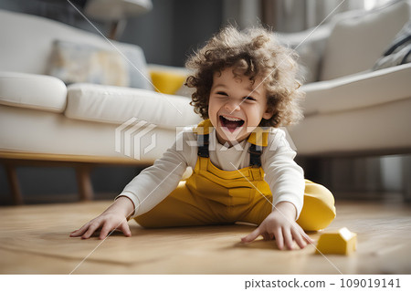 Happy child in yellow overalls with wavy hair plays with colorful toy blocks on the floor in a bright living room. Educational game for kids 109019141