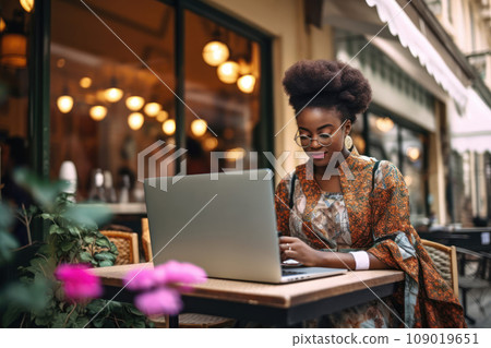 Fashionable African woman with glasses working on laptop at a stylish outdoor cafe. Generative AI 109019651