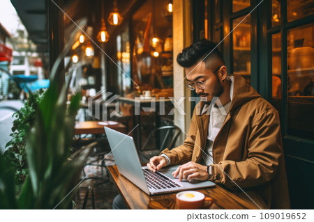 Young Asian man focused on work using laptop in a cozy outdoor cafe. Generative AI 109019652