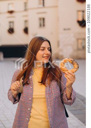 Attractive young female 30s tourist with backpack is holding prezel, traditional polish snack on the Market square in Krakow. Traveling Europe in spring. Selective focus. High quality photo Attractive young female 30s tourist with backpack is holding prezel, traditional polish snack on the Market square in Krakow. Traveling Europe in spring. Selective focus. High quality photo 109022186