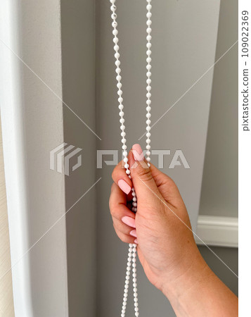 A female hand holding a beaded chain for the blinds. High quality photo A female hand holding a beaded chain for the blinds. High quality photo 109022369