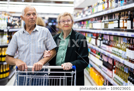Mature couple chooses bottle of wine in alcohol section of supermarket 109023601