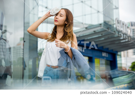 Asian beautiful business woman drying sweat her face with cloth in warm summer day hot weather, Female having sunstroke skin damage from sun UV city air pollution outdoors on street 109024040