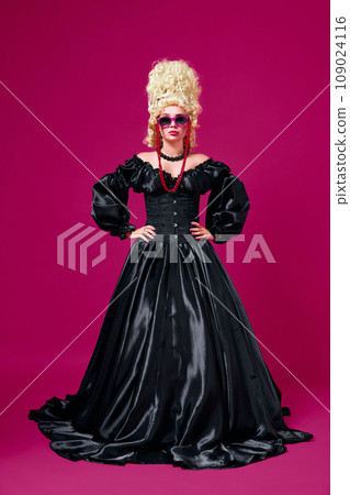 Full length portrait of young girl dressed like medieval person in black old-fashioned dress with modern accessories against magenta background. 109024116
