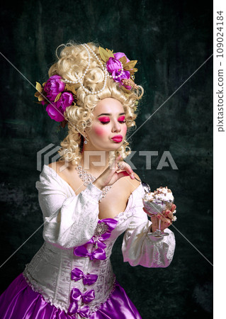 Young woman, queen with bright makeup and retro hairstyle tasting cold and sweet dessert against vintage background. Young woman, queen with bright makeup and retro hairstyle tasting cold and sweet dessert against vintage background. 109024184