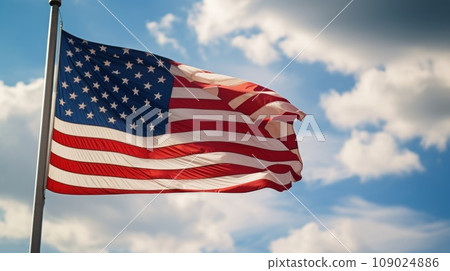 a flag waving in the wind with a blurred background of blue sky and clouds. a flag waving in the wind with a blurred background of blue sky and clouds. 109024886