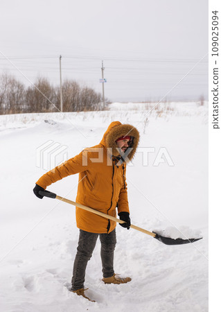 A man cleans and clears the snow in front of the house on frosty day. Cleaning the street from snow on a winter day. Snowfall and severe snowstorm in winter. 109025094