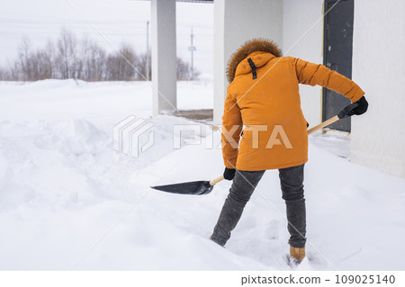 Young man clearing snow in his backyard village house with shovel. Remove snow from the sidewalk. Young man clearing snow in his backyard village house with shovel. Remove snow from the sidewalk. 109025140