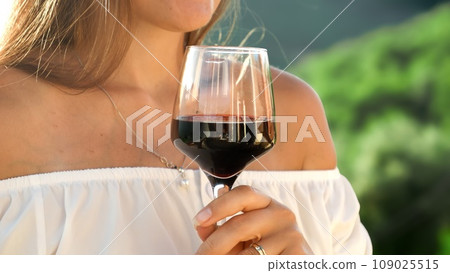 Closeup of woman stirring red wine in glass while standing on villa balcony or terrace 109025515