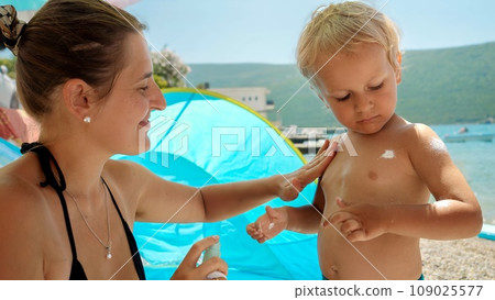Closeup of mother and baby son using sunscreen lotion while having time on sea beach Closeup of mother and baby son using sunscreen lotion while having time on sea beach 109025577
