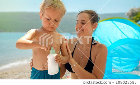 Portrait of little baby boy with mother applying sunscreen UV protection lotion on sea beach during summer holiday vacation Portrait of little baby boy with mother applying sunscreen UV protection lotion on sea beach during summer holiday vacation 109025583