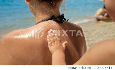 Closeup of child helping his mother applying sunscreen UV protection lotion on sea beach during summer holiday vacation Closeup of child helping his mother applying sunscreen UV protection lotion on sea beach during summer holiday vacation 109025613