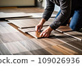Male worker installing new wooden laminate flooring. The combination of wood panels of laminate and ceramic tiles in the form of honeycomb. Kitchen renovation. 109026936