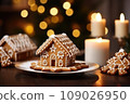 Gingerbread house on table. Defocused lights of Christmas garland. Evening in the living room. Holiday mood.  109026950