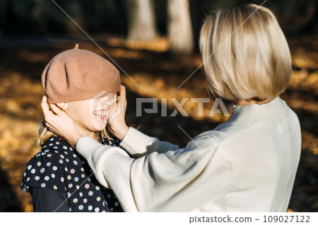 Autumn family walk. Heartwarming moment of smiling mother lovingly placing autumn leaf in daughters girls hair. Happy Mother and teen girl daughter in cozy sweaters, simple joys of the fall season. Autumn family walk. Heartwarming moment of smiling mother lovingly placing autumn leaf in daughters girls hair. Happy Mother and teen girl daughter in cozy sweaters, simple joys of the fall season. 109027122