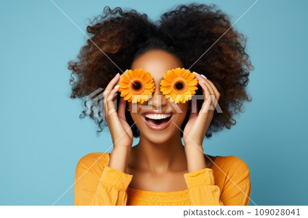 African girl in orange shirt with orange flowers smiles on the blue background 109028041