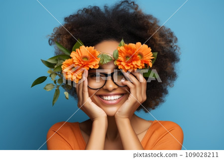 African girl with glasses in orange shirt with orange flowers smiles on the blue background 109028211