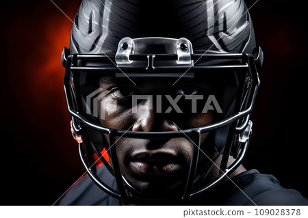 American football player of African descent in dark uniform and helmet on a dark background 109028378