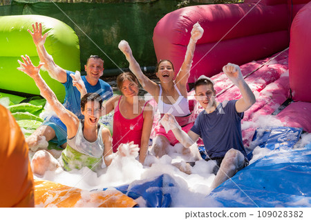 Cheerful friends picking up balls in inflatable pool full of foam 109028382