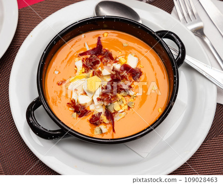 There is large portion of soup salmorejo cordoba decorated with hill of ham and egg chips 109028463