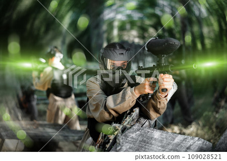 Paintball player in protective uniform aiming and shooting with guns 109028521