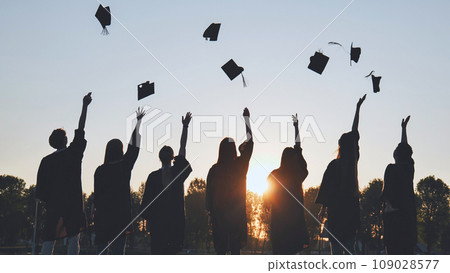 Silhouettes of Happy college graduates tossing their caps up at sunset. 109028577