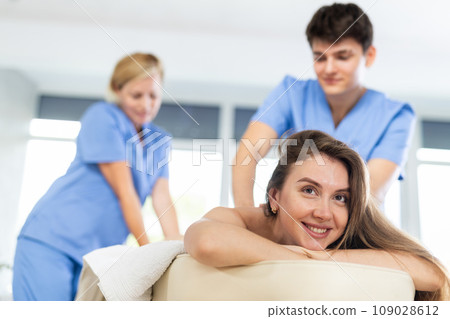 Cheerful young woman getting professional massage from two therapists 109028612