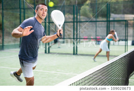 Man hitting ball with left-handed forehand while playing padel on open court 109028673