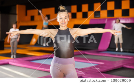 Portrait of fit active woman in sport clothes enjoying weekend time on trampolines indoors in entertainment center 109029009