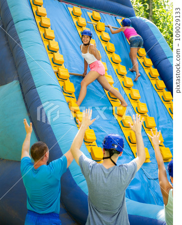 Happy girl competing in climbing with wood poles on inflatable slide Happy girl competing in climbing with wood poles on inflatable slide 109029133