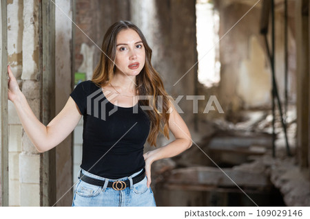 Young woman in jeans and black tee shirt posing in ruined building Young woman in jeans and black tee shirt posing in ruined building 109029146