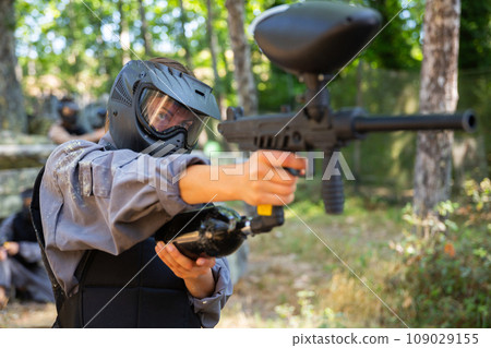 Woman in protective clothes and helmet aiming with paintball marker Woman in protective clothes and helmet aiming with paintball marker 109029155