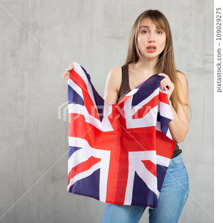 Sad young woman holding flag of Great Britain against unicoloured background 109029275