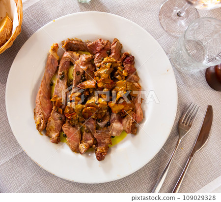 Sliced tagliata steak with sauteed white mushrooms on plate 109029328