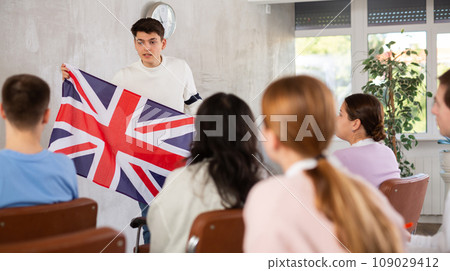 Young teacher holding flag of Great Britain in front of group of students 109029412