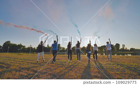 A group of friends spraying multi-colored smoke at sunset. 109029775