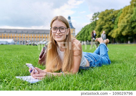 Young student girl lying on grass, educational building background Young student girl lying on grass, educational building background 109029796