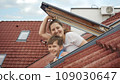 Happy smiling mother with son opens attic windows and looks outdoor. Concept of family happiness, parents with kids, moving to a new house. 109030647