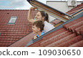 Happiness of a mother and her son as they open attic windows and peer outdoors, symbolizing the essence of family joy, parents with their children, and the excitement of a new home 109030650