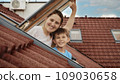 Delight of a mother and her son as they open attic windows and enjoy the view outside, illustrating the idea of family joy, parents sharing moments with their kids, and the excitement of relocating to 109030658